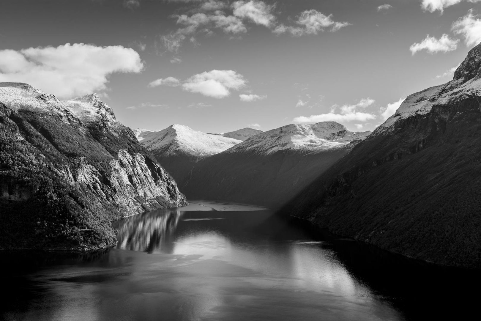 Fjordlandskap med snöklädda berg och speglande vatten i svartvitt.
