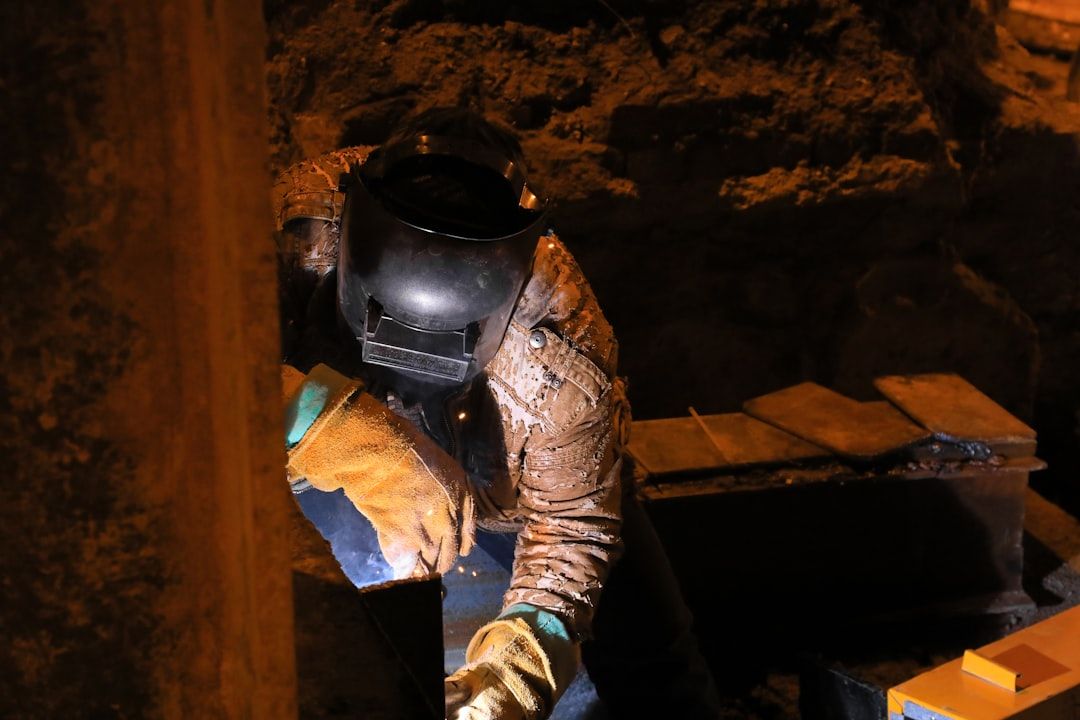 Arbetare svetsar i en tunnel, klädd i skyddsutrustning. Svetslågan lyser upp mörkret.